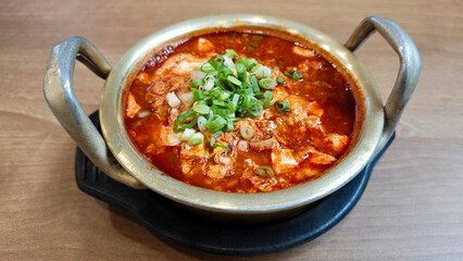 Close-up of Sundubu Jjigae Korean Soft Tofu Stew with Green Onion Garnish in a Traditional Brass Pot on a Wooden Table