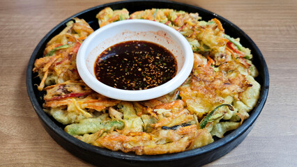 Close-up of Korean Haemul Pajeon Seafood Pancake with Soy Dipping Sauce on Black Plate on Wooden Table