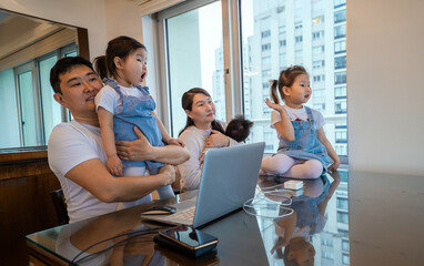 A family of four is sitting at a table with a laptop open