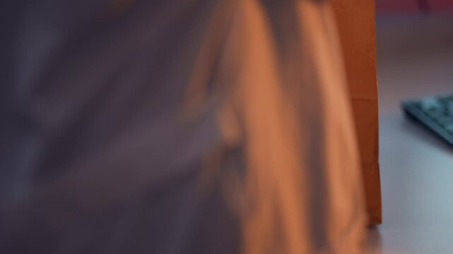 Woman comes to office with bought lunch in paper packet and cup of coffee. Lady is putting take out food on work desk in front of computer filmed in closeup slow motion. Concept of eating at job