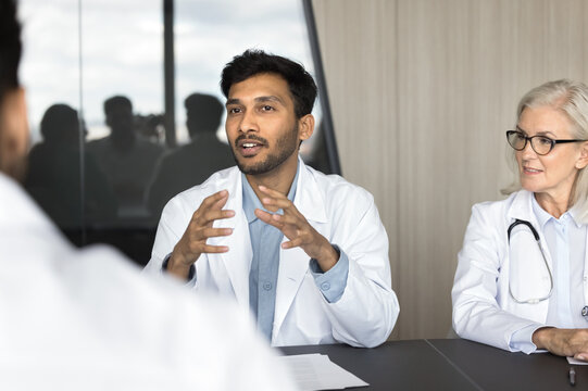 Millennial Indian male doctor speaking, sharing insights, presenting information during group seminar with colleagues, engaged in professional interaction and knowledge exchange. Medical council event