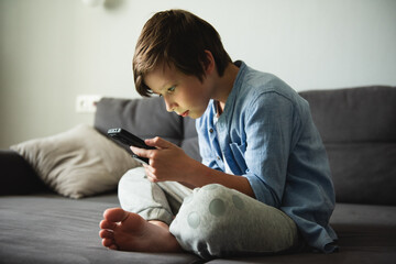 Boy with a serious face on the couch communicates on Internet. Child gadget addiction