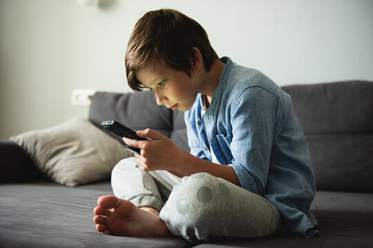 Boy with a serious face on the couch communicates on Internet. Child gadget addiction