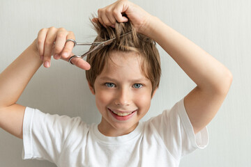 Cute and happy boy cut his long hair himself. Closeup portrait of happy young child having his hair cut with scissors at home