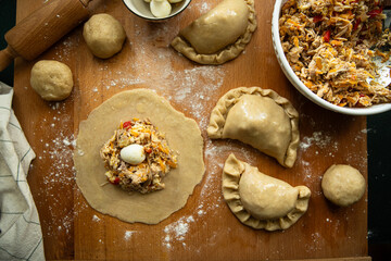 Step by step process of preparing homemade empanadas stuffed with meat, vegetables and quail egg. Rolled dough with filling on wooden board.
