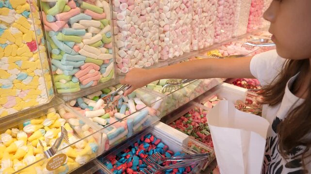 Little girl daughter picking up sweet candies in a candy shop with colorful interior
