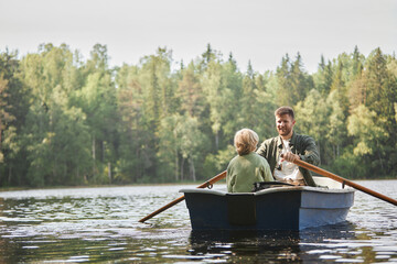 Father and child enjoying tranquil boat ride on lake surrounded by lush, green forest with calm water reflecting trees. Enjoying serene and peaceful environment while bonding