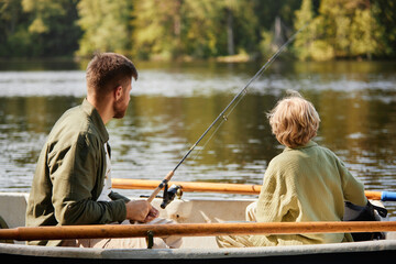 Two individuals enjoying serene fishing experience in a boat on lake surrounded by lush greenery...