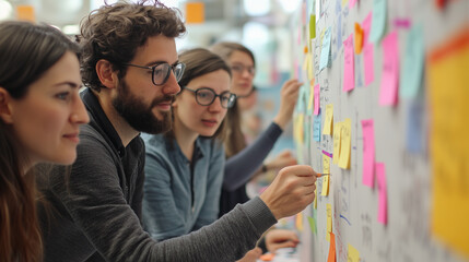 Young entrepreneurs collaborate and generate new concepts using colorful sticky notes on a whiteboard during a brainstorming session