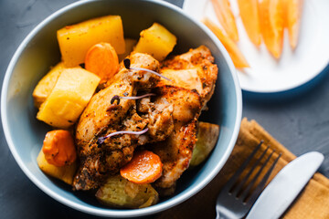Close-up.Chicken fried with rustic potatoes in a blue bowl with tomatoes on a plate, napkin and fork, knife.
