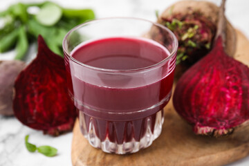 Fresh beet juice in glass and ripe vegetables on table, closeup
