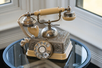 Antique rotary telephone on a table by windows.