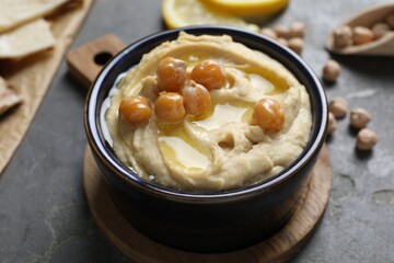 Delicious hummus with olive oil and chickpeas in bowl on grey table, closeup