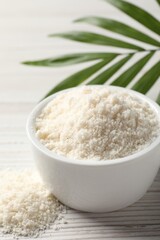 Fresh coconut flour in bowl and palm leaf on white wooden table