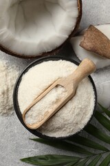 Coconut flour in bowl, scoop, fresh fruits and leaf on light grey table, flat lay