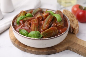 Tasty stew with okra, tomato sauce and basil on white tiled table, closeup