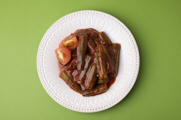 Tasty stew with okra and tomato sauce on light green background, top view
