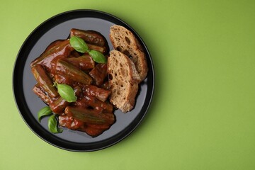 Tasty stew with okra, tomato sauce, bread and basil on light green background, top view. Space for text