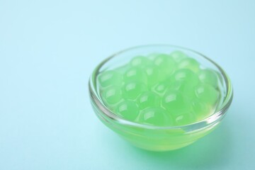 Bright tapioca pearls in bowl on light blue background, closeup