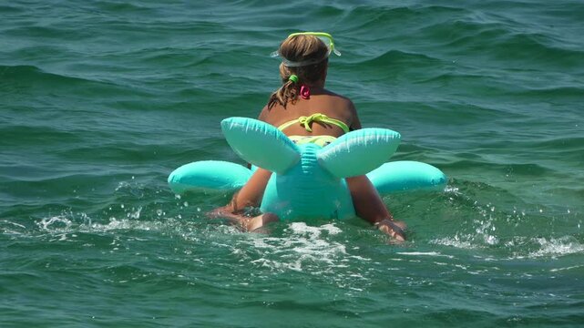 Girl, Inflatable dolphin, Sea: Young girl floats on a turquoise inflatable in clear water during a summer day.