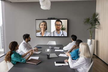 Mature female patient displayed on screen during medical council with internists. Group of doctors participate in on-line communication with diverse colleagues, share opinions, skills and knowledge