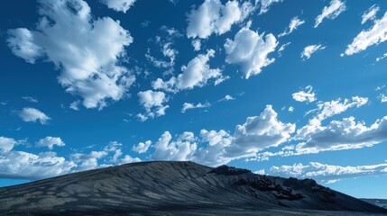 Fototapeta premium A crisp, clear day with fluffy, cumulus clouds casting moving shadows over the slopes of a black mountain, enhancing its rugged texture.