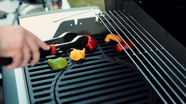 Slow-motion of a hand managing sliced vegetables with tongs on the barbeque grill