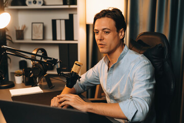 Host channel smart broadcaster talking on live social media application searching on laptop, broadcasting streamer wearing headphone using mic at modern home office studio in warm lighting. Pecuniary.