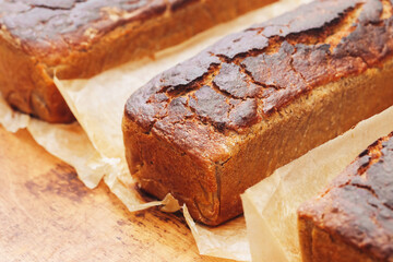 Homemade bread on a wooden kneading board. Bread wrapped in rustic brown paper. Traditional baking with a warm and inviting atmosphere in a cozy kitchen setting. Bread baking craft.