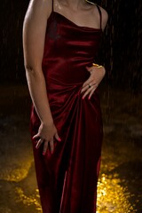 A girl without a face in a wet red dress walks down the street during the rain.