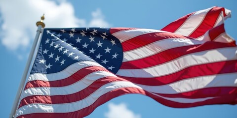 Obraz premium American flag waving against a blue sky with white clouds during midday