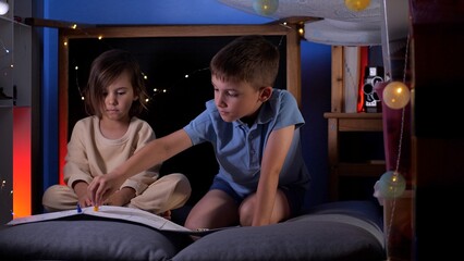 Two young children playing board game in pillow fort