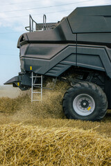 Fototapeta premium Side view of a combine harvester in a wheat field, focusing on the machinery's tire and chaff dispersion. Advanced farming technology during harvest season. Agricultural efficiency. Vertical photo