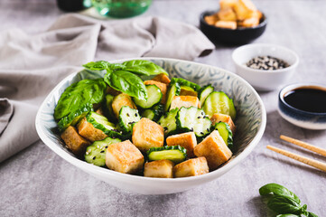 Fresh cucumber and fried tofu salad with basil leaves in bowl on table