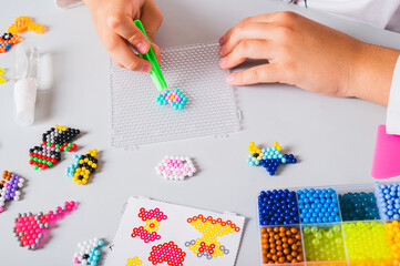 A girl makes a pattern of aqua beads using tweezers on a pegboard
