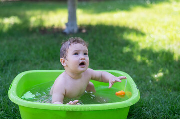 Unhappy boy bathes in a basin outdoors in summer.