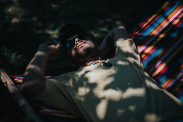 Man lying on a colorful hammock, basking under dappled sunlight. Enjoying a tranquil outdoor moment, emphasizing relaxation and leisure.