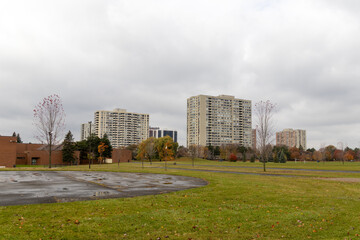 Overcast sky over urban park with scattered autumn leaves - high-rise apartment buildings - wet asphalt parking lot. Taken in Toronto, Canada.