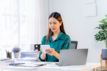 Focused Female Entrepreneur: Young Asian woman meticulously manages finances at her home office,...