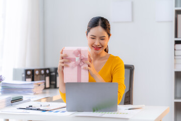 Virtual Surprise Celebration: Joyful Asian businesswoman showing gift box during video call in office. 