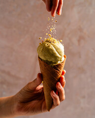 hand holding a scoop of pistachio ice cream and pistachio being sprinkled 