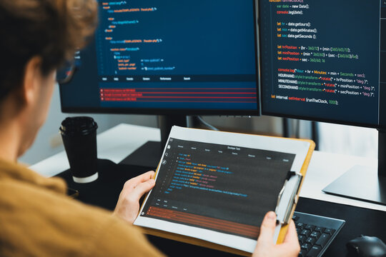 Working IT developer reading coding on document paper software with screens pc at modern office on coding application screens, creating updated program firmware information version concept. Gusher.