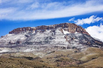 Red butte in the Bighorn Mountains Wyoming dusted with snow and a blue clouded sky.