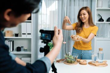Asian beautiful woman food specialist presenting healthy meal wholegrain bun bread basket on live channel recorded video camera by smart cameraman streaming lifestyle social media online. Infobahn.