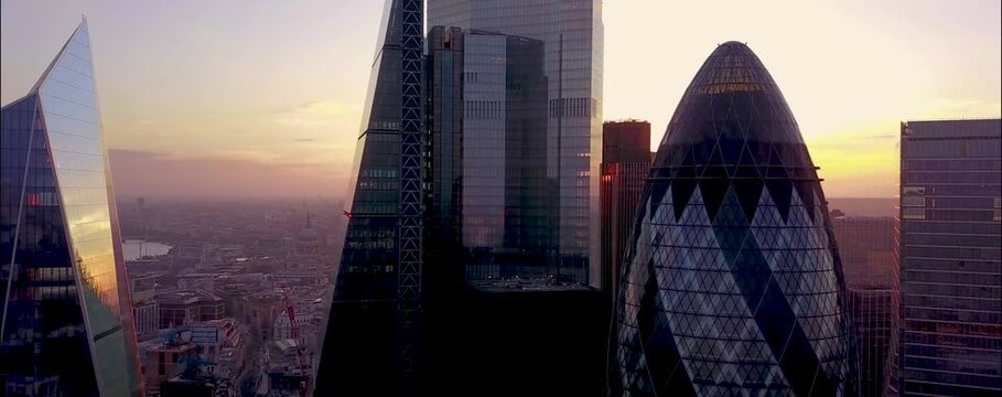 
As the sun begins to set over London, the city's iconic skyline is bathed in a warm, golden glow. From a drone's aerial perspective, the skyscrapers rise majestically, their glass facades reflecting 