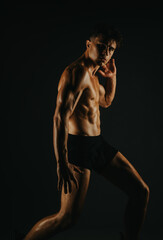 Obraz premium Muscular male athlete posing in a dark room showcasing strength, fitness, and a well-defined physique. Ideal image for health and fitness related content.