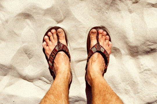 Man feets slippers standing on the beach sand