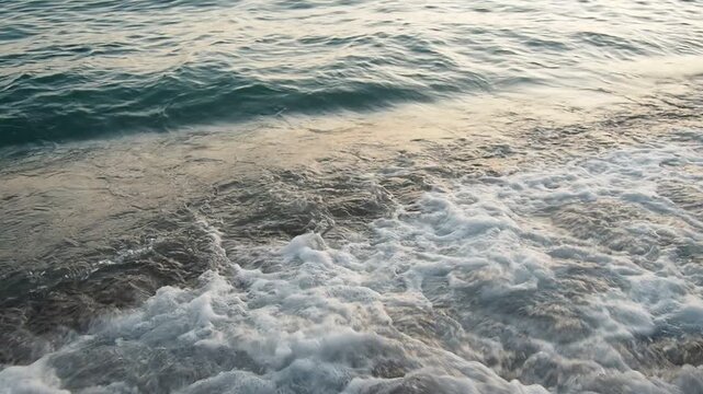 Waves gently lap at shore during stunning sunset over ocean. Golden sunlight reflects off waves as they roll onto shore, creating tranquil atmosphere at sunset by sea. Montenegro summer Canj