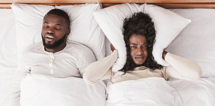 Snoring husband. Unhappy black woman covering her ears with pillow, can not handle loud snore of her partner, top view