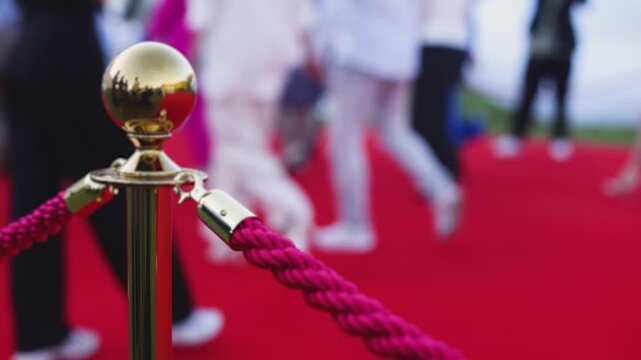 Red carpet with ropes and golden barriers on a luxury party entrance, cinema premiere film festival event award gala ceremony, wealthy rich guests arriving, outdoor decoration elements, summer day